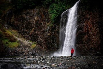 Franklin Falls in with Jonathan Gulingan standing in the foreground. The waterfall is full and crashing into the rocks.